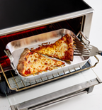 Cheese pizza slices reheating in a toaster oven on a silver baking pan with a spatula
