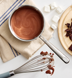 Homemade hot chocolate in saucepan with marshmallows, chopped dark chocolate, and whisk