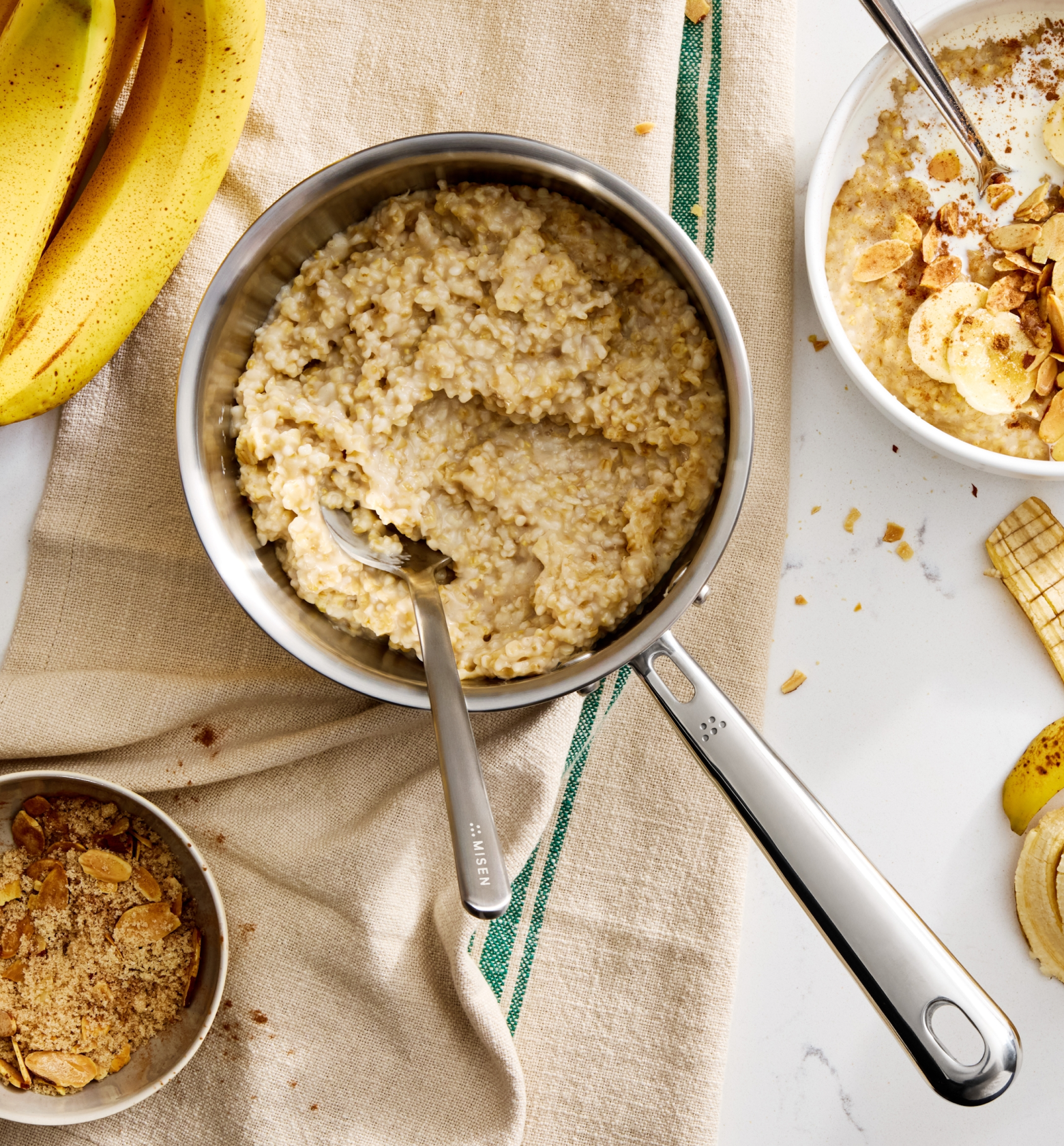 Creamy oatmeal in Misen stainless saucepan with banana slices, brown sugar, and toasted almonds