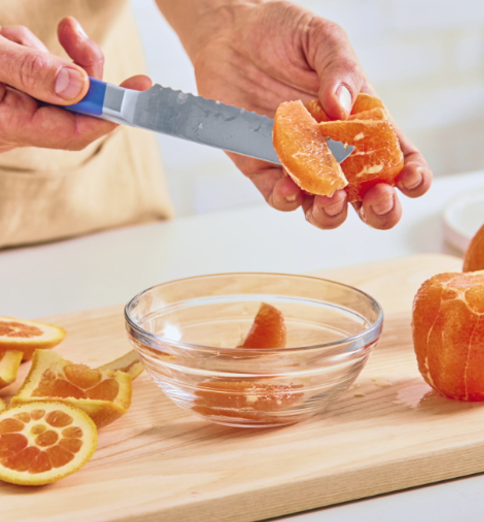 Hands segmenting a peeled orange over a glass bowl on a wooden cutting board