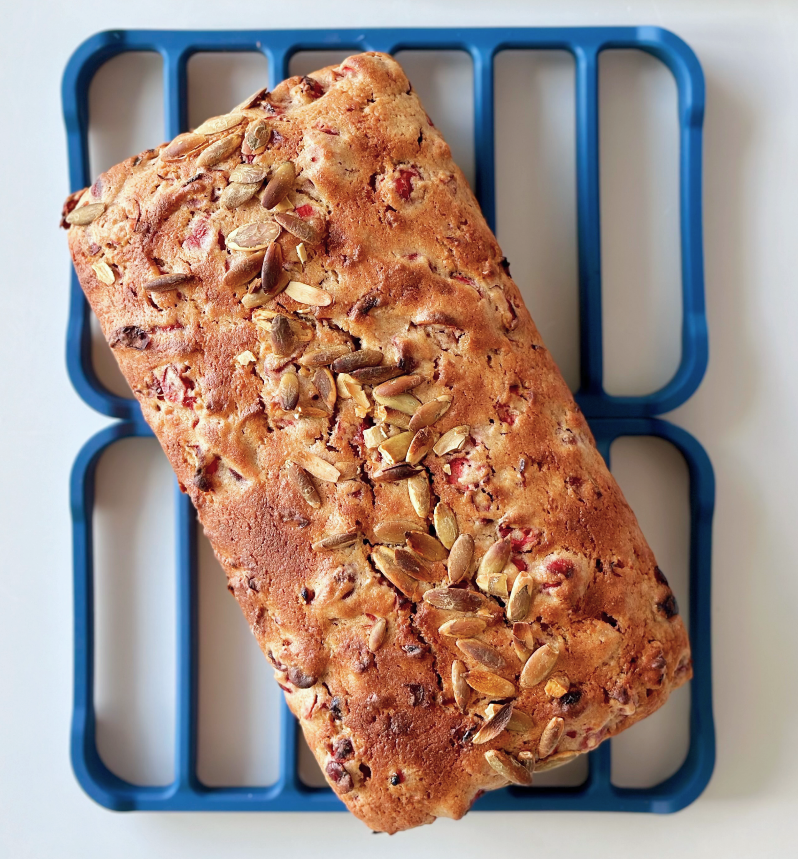 Homemade cranberry seed loaf bread topped with pumpkin seeds on blue cooling rack