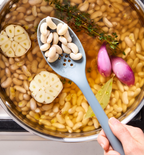 White beans simmering in pot with garlic, shallots, thyme, and bay leaf