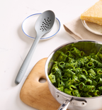 Rigatoni pasta with green pesto sauce in stainless steel pan with slotted spoon and Parmesan