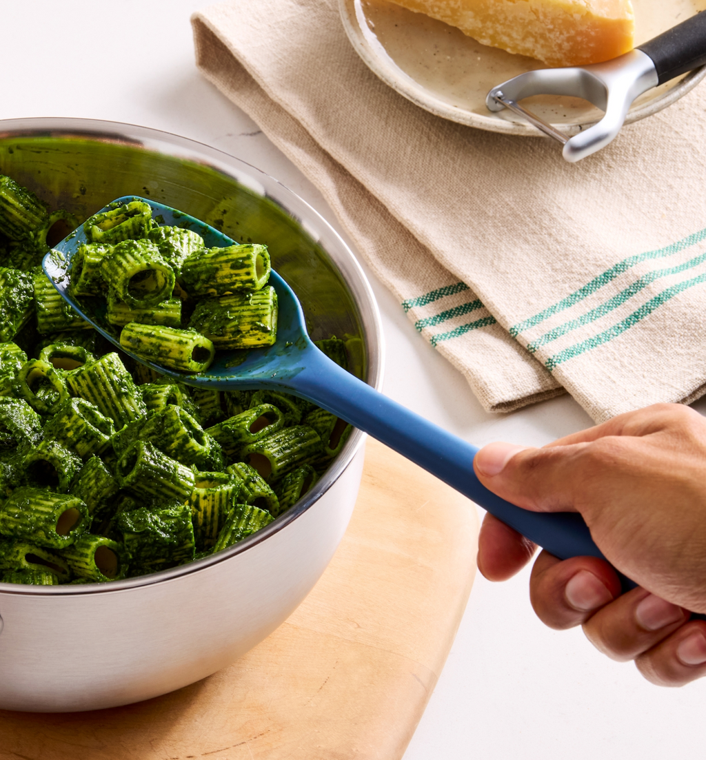 Rigatoni pasta tossed in vibrant green pesto sauce served in a stainless steel bowl