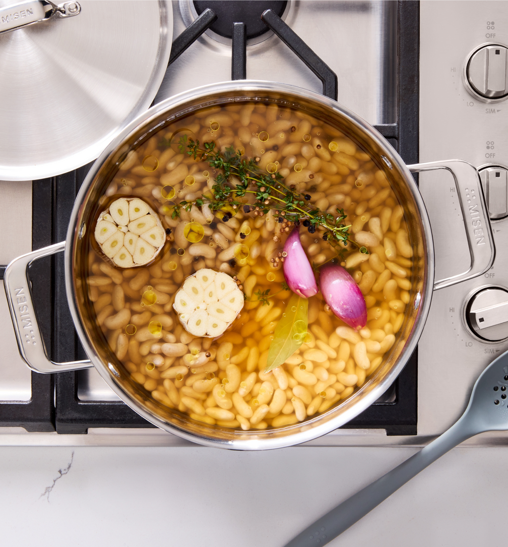 White beans simmering in Misen stainless steel pot with garlic, shallots, thyme, and bay leaf