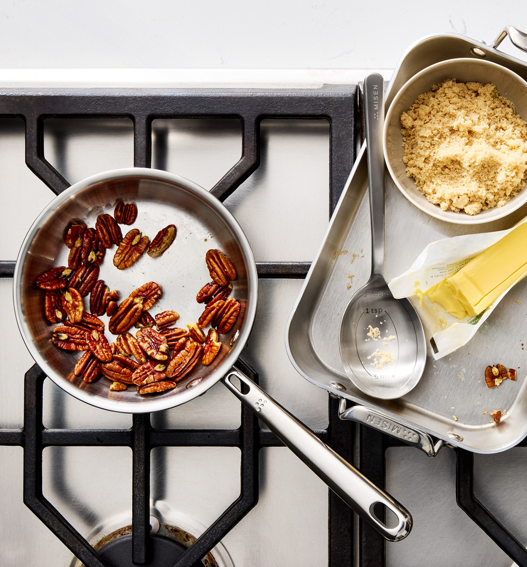 Misen stainless steel cookware with toasted pecans, brown sugar, butter, and measuring spoon on gas stovetop
