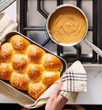 Freshly baked dinner rolls with sea salt in baking pan next to warm cheese sauce on stovetop