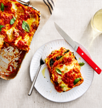 Homemade vegetarian lasagna slice on white plate with tomato sauce, melted mozzarella, and fresh basil