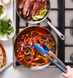 Steak fajitas with sautéed peppers and onions cooking in stainless steel pans on gas stovetop