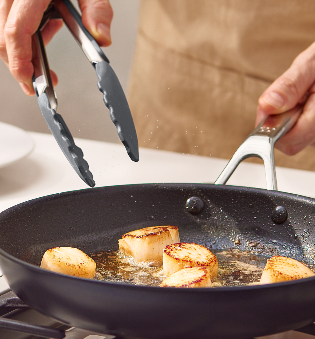 Searing sea scallops in a nonstick skillet with kitchen tongs