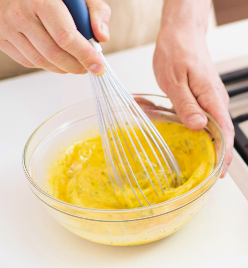 Hands whisking bright yellow egg mixture in a glass bowl