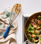 Sautéed Brussels sprouts in a skillet on stovetop with a blue-handled whisk and kitchen towel