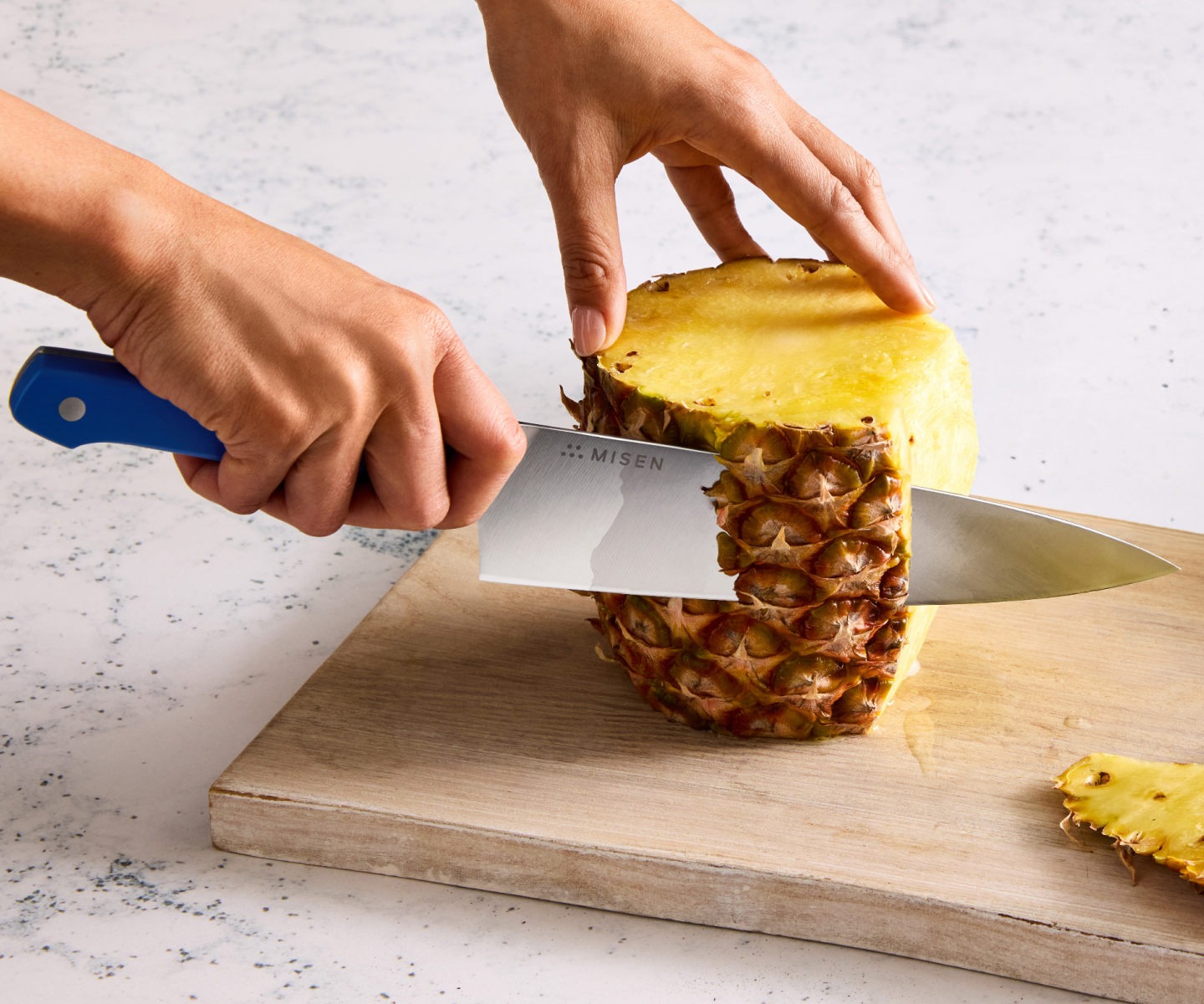 Misen chef's knife cutting fresh pineapple skin on wooden cutting board