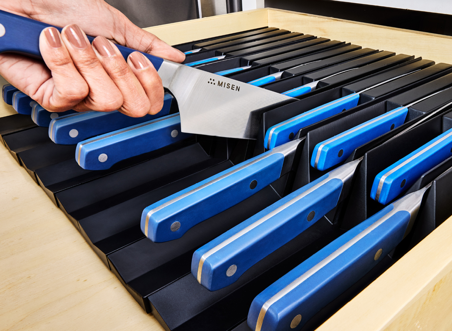 Several pieces of large & small black Modular Knife storage pieces inside a kitchen drawer with various blue Misen kitchen Knives.
