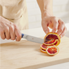 Using a blue, Misen, five inch, short serrated knife to cut a blood orange