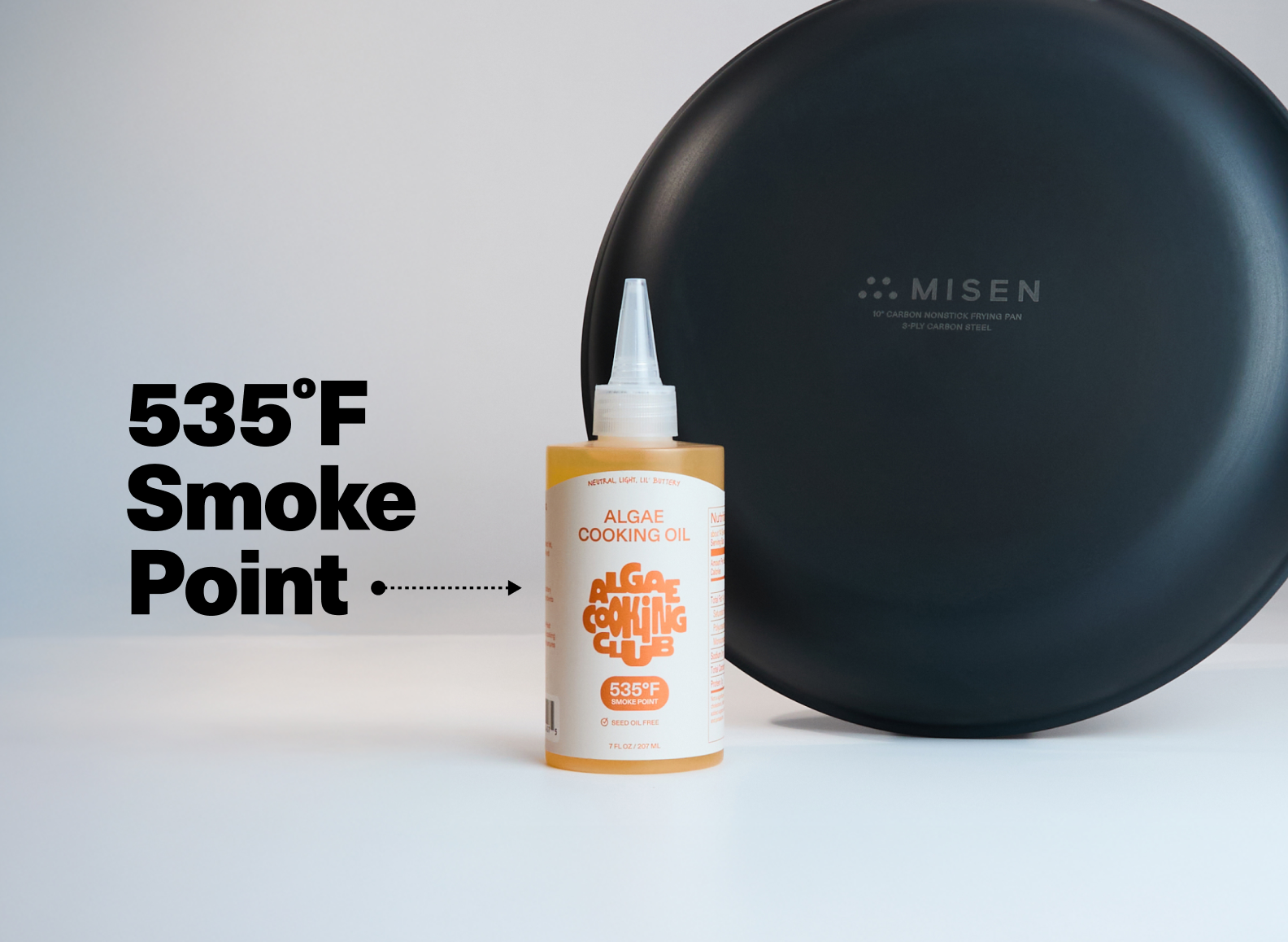 A bottle of Algae Cooking Club cooking oil is next to a 10" Misen Carbon Nonstick™ Pan. The oil has a smoke point of 535°F.
