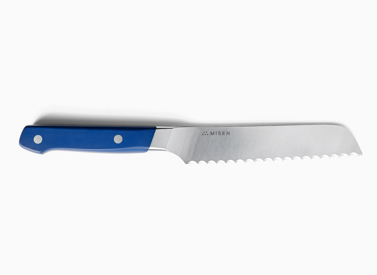 A top-down view of a black-handled 5 inch Serrated Knife 2.0 against a white background. The knife is positioned horizontally with the handle on the left and the serrated blade extending to the right. The ACUTO440 steel blade is silver-toned and features the "MISEN" logo and name. The handle is a rich blue with two silver rivets visible.