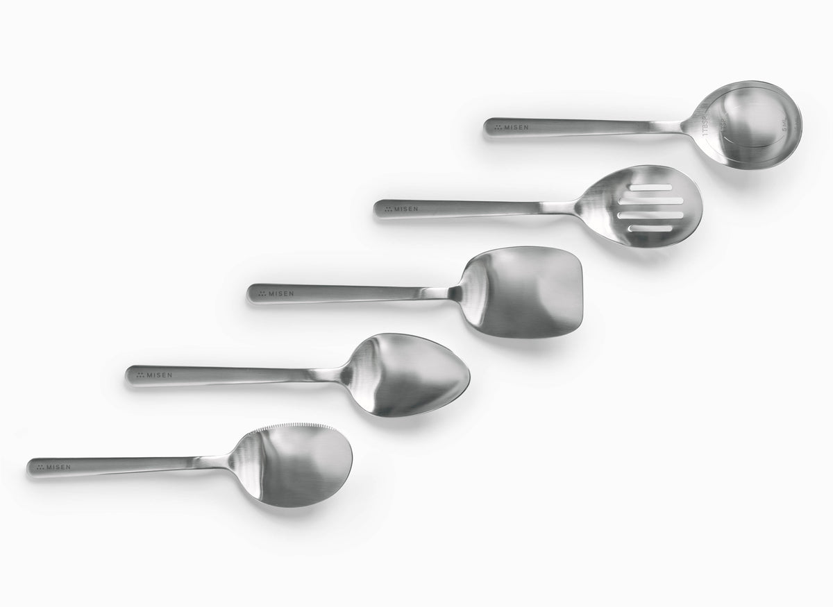 The image displays five stainless steel chef spoons from the brand Misen, arranged diagonally on a white background. From top to bottom, the utensils are: a measuring chef spoon, a slotted chef spoon, a rectangular scraper chef spoon, an oval plating chef spoon, and a serrated chef spoon. Each utensil has "MISEN" embossed on its handle.