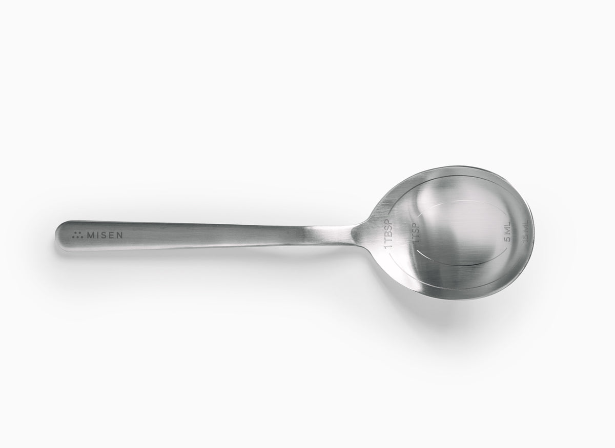 A stainless steel measuring spoon with the brand name "MISEN" engraved on the handle. The bowl of the spoon has markings for 1 TBSP, 1 TSP, 5 ML and 15 ML.