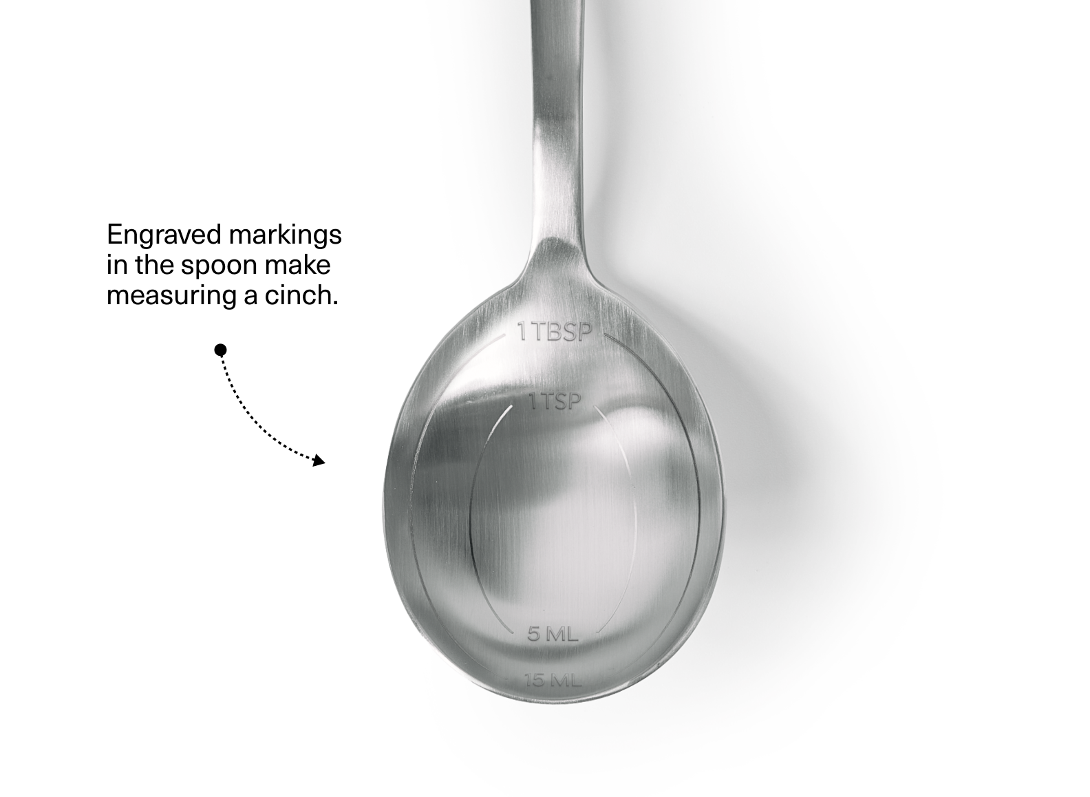 A stainless steel measuring spoon is shown from above, with engraved measurements visible inside the bowl. The visible measurements are "1 TBSP", "1 TSP", "5 ML", and "15 ML". Text next to the spoon reads, "Engraved markings in the spoon make measuring a cinch."