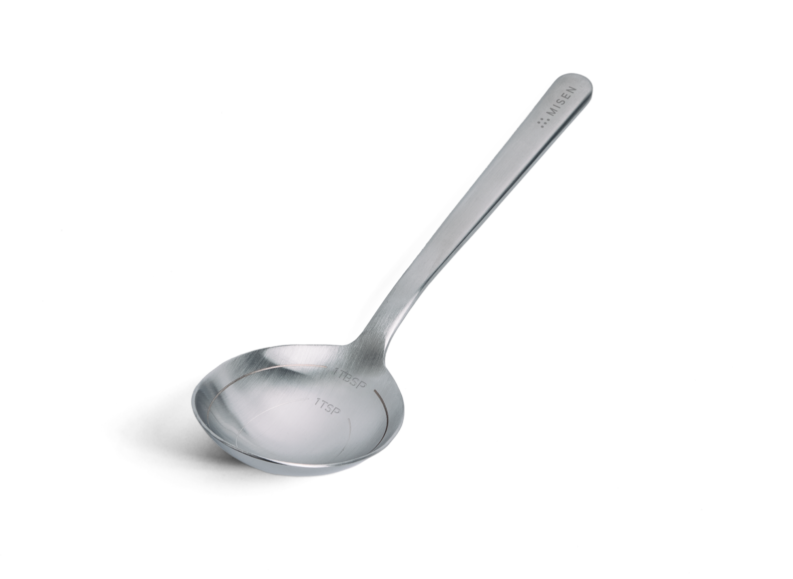 A stainless steel measuring spoon is positioned at an angle on a white background, with its bowl facing towards the lower left of the image. Engraved markings inside the bowl indicate "1 TBSP" and "1 TSP". The brand name "MISEN" is visible on the handle.