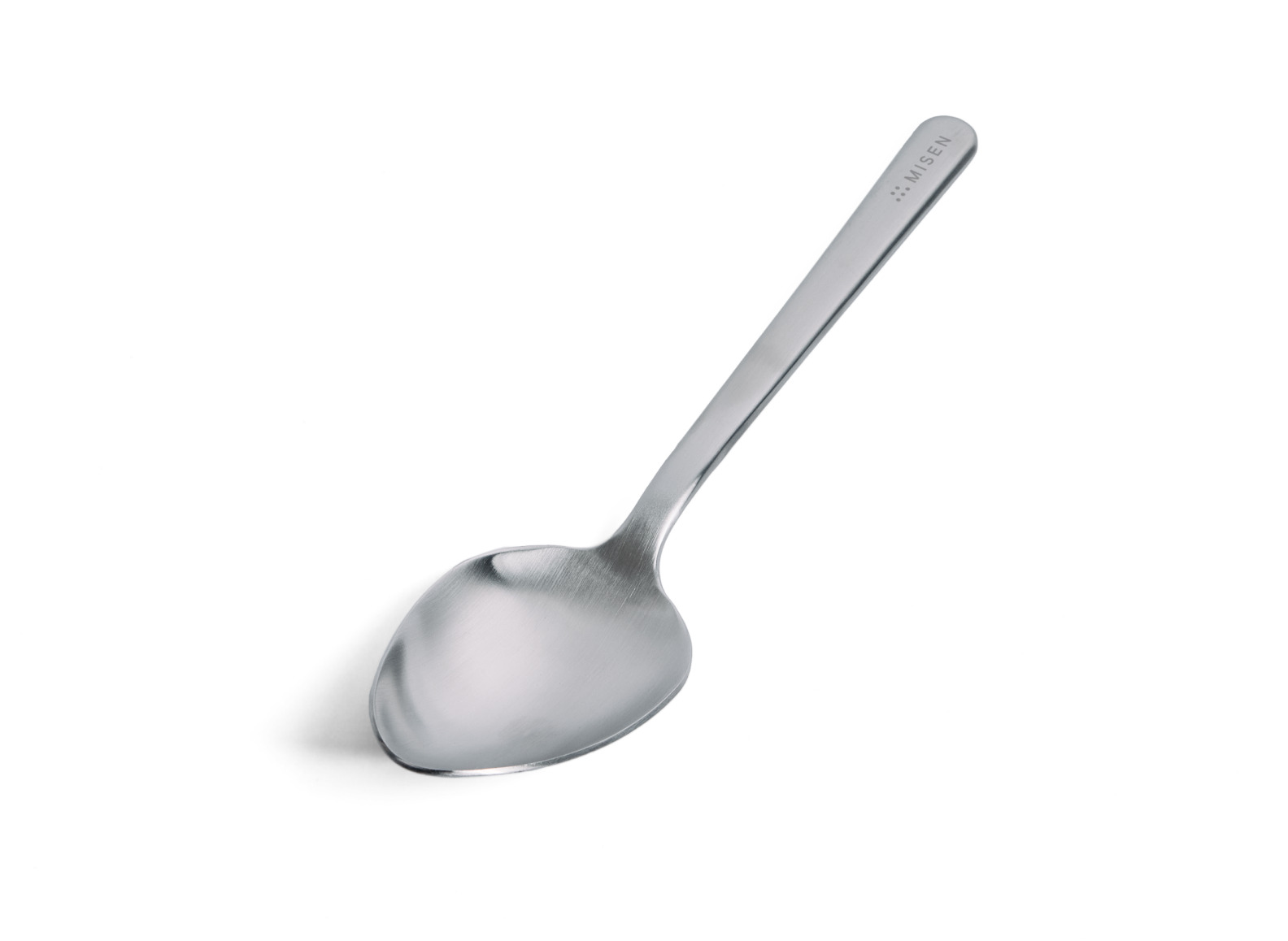 A Misen stainless steel plating spoon is positioned diagonally against a white background, with its handle extending towards the upper right. The spoon has a shallow, oval-shaped bowl with a polished finish and a long, slender handle with a matte finish. The word "MISEN" is subtly debossed on the upper right side of the handle, near its end.