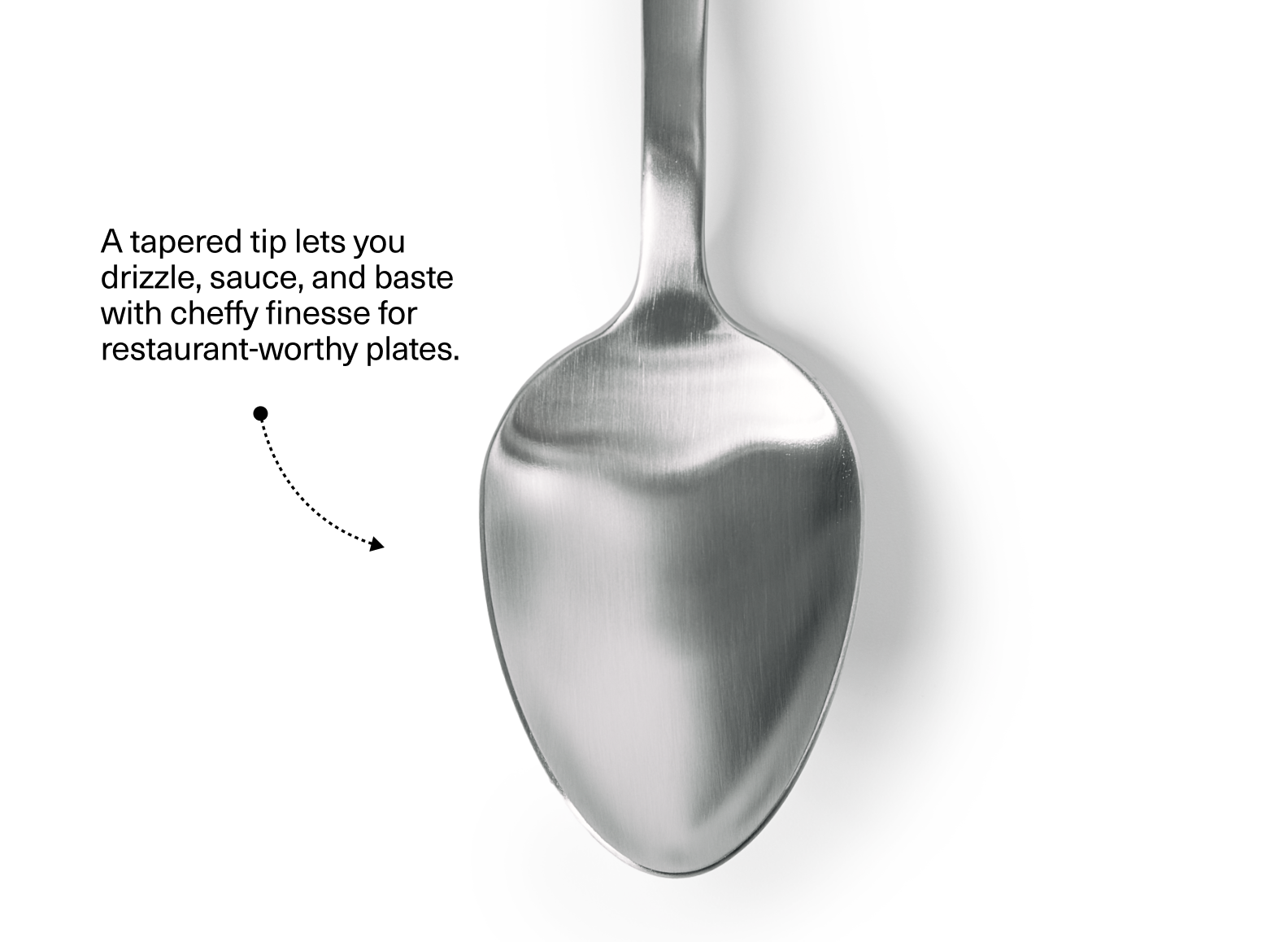 The image shows the oval-shaped bowl of a stainless steel plating spoon, positioned vertically against a white background. The spoon bowl has a polished, reflective finish and a tapered tip. To the left of the spoon, there is text that reads: "A tapered tip lets you drizzle, sauce, and baste with cheffy finesse for restaurant-worthy plates." Below the text, a dotted line with an arrow points towards the tip of the spoon bowl.