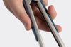 Close up view of a hand holding a blue pair of Misen Tongs, seen on a white background.