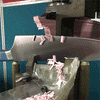 Large chef knife blade clamped, slicing thin stacked pink plastic strips that fall into a clear plastic bag.