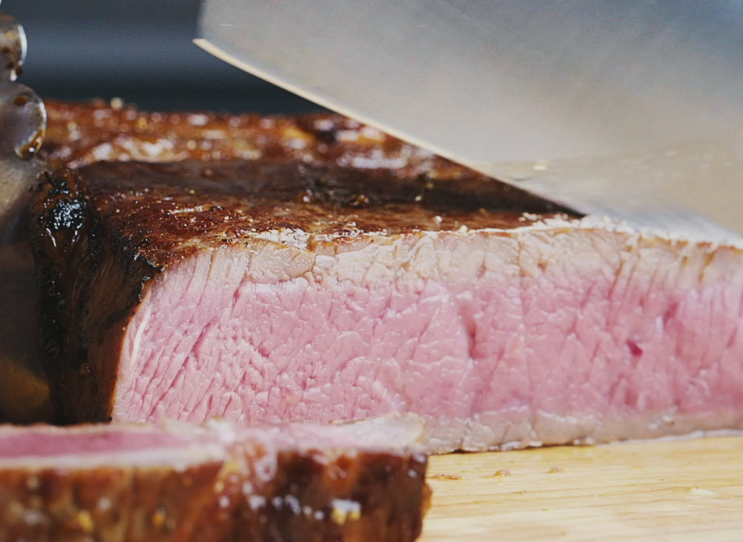 A Misen 8 inch Chef's Knife in blue slicing through a medium steak, held by a pair of stainless steel tongs.
