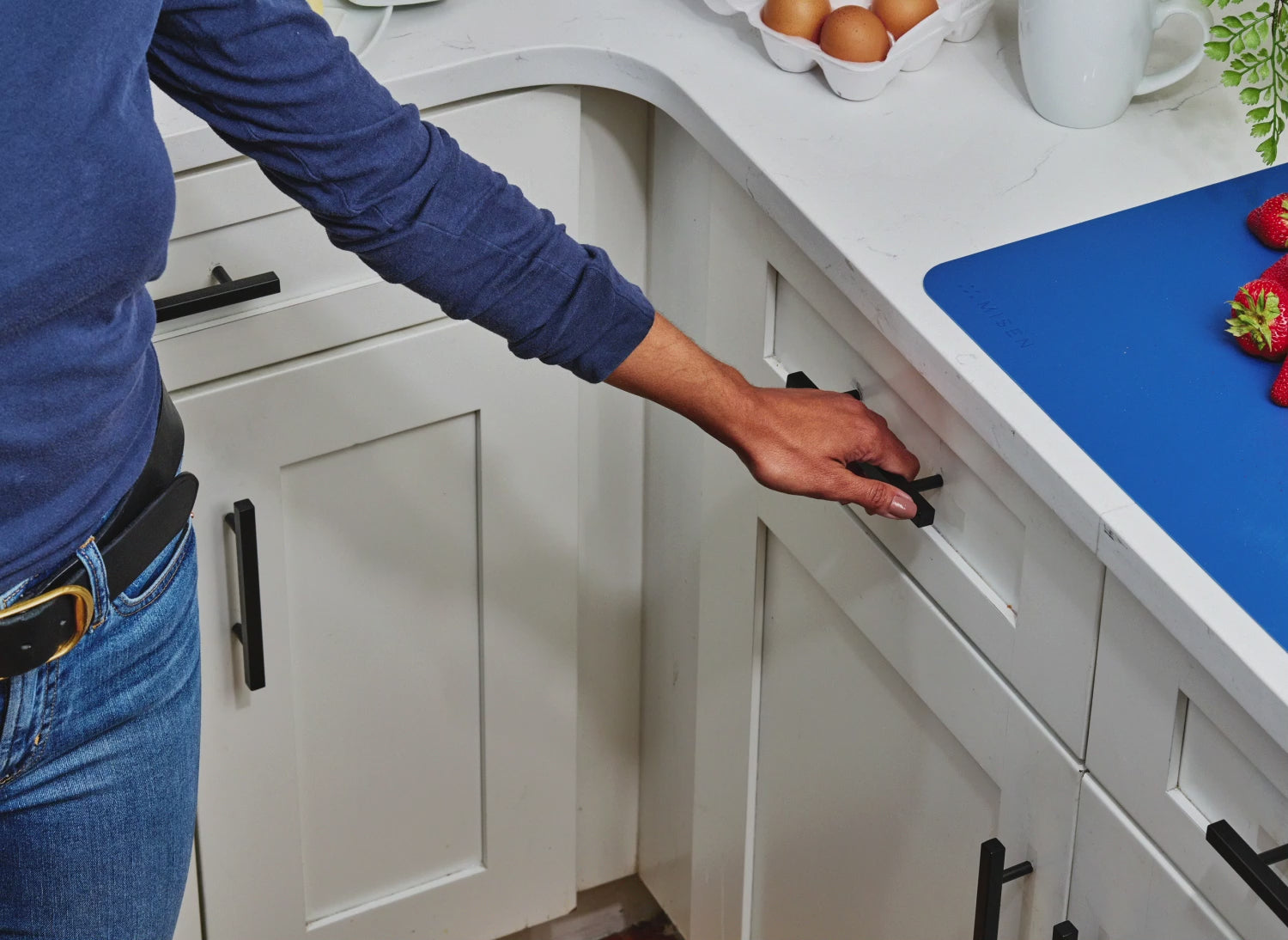 Opening a white kitchen drawer to reveal white Modular Knife Storage with green Misen knives in the large lots and blue Misen knives in the small slots.
