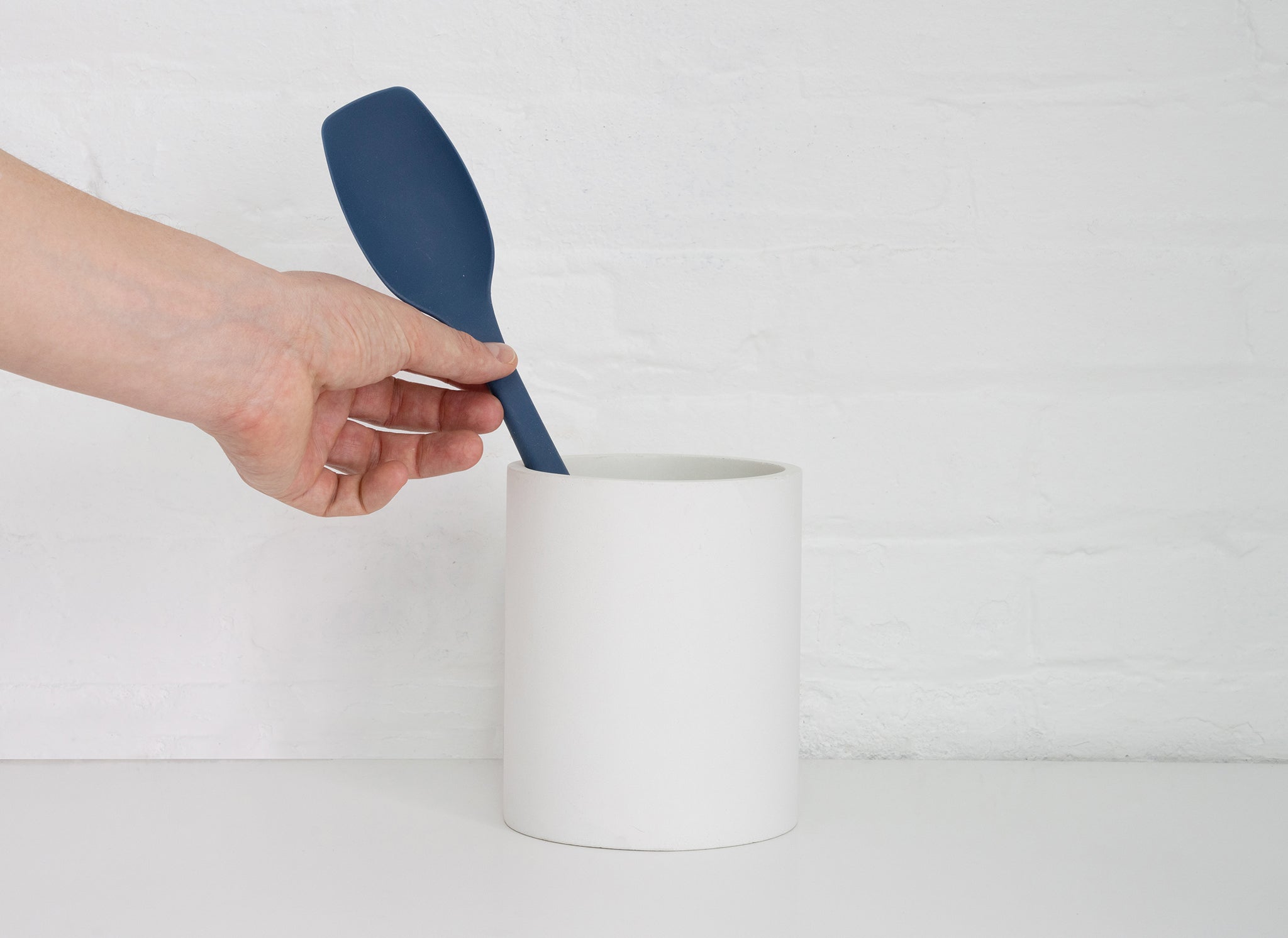 A hand grabbing a Blue Misen Spoontula from a White Misen Prep Tool Holder on a white countertop.